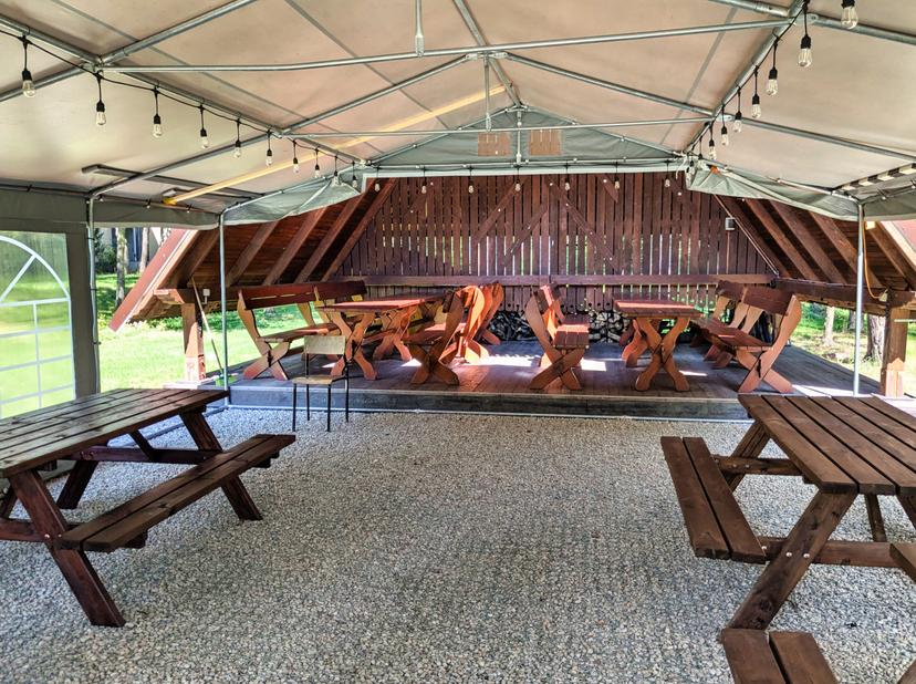 Drewniana wiata przykryta namiotem z drewnianymi stołami i ławkami do spożywania posiłków